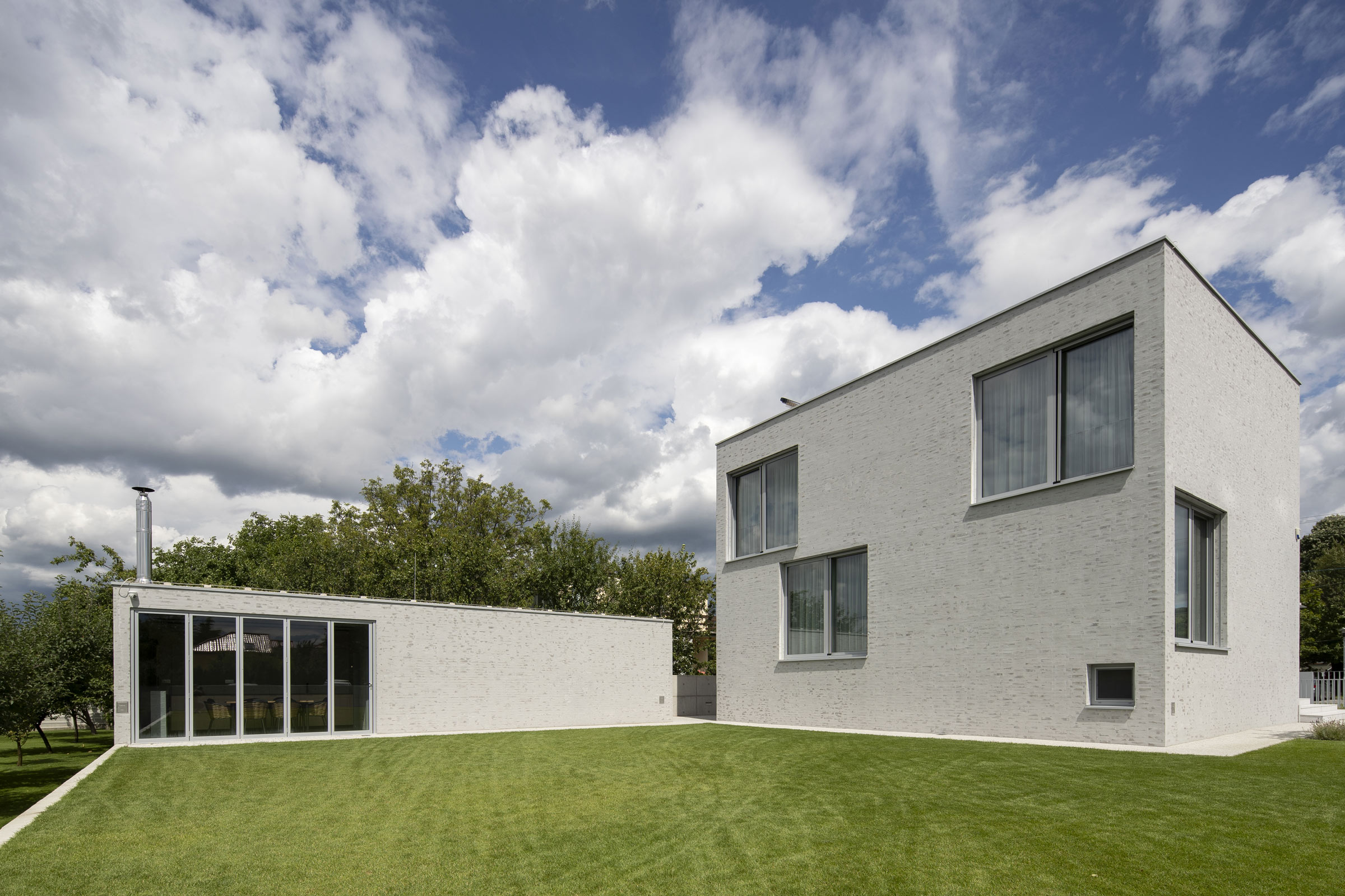 Fasáda rodinného domu z cihlového obkladu a broušené omítky s jemnou, vrstvenou strukturou.